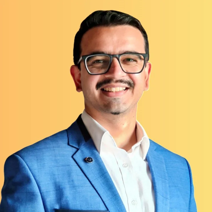 Smiling person in blue suit and glasses against a yellow background, exuding a cheerful and professional vibe. Doctor